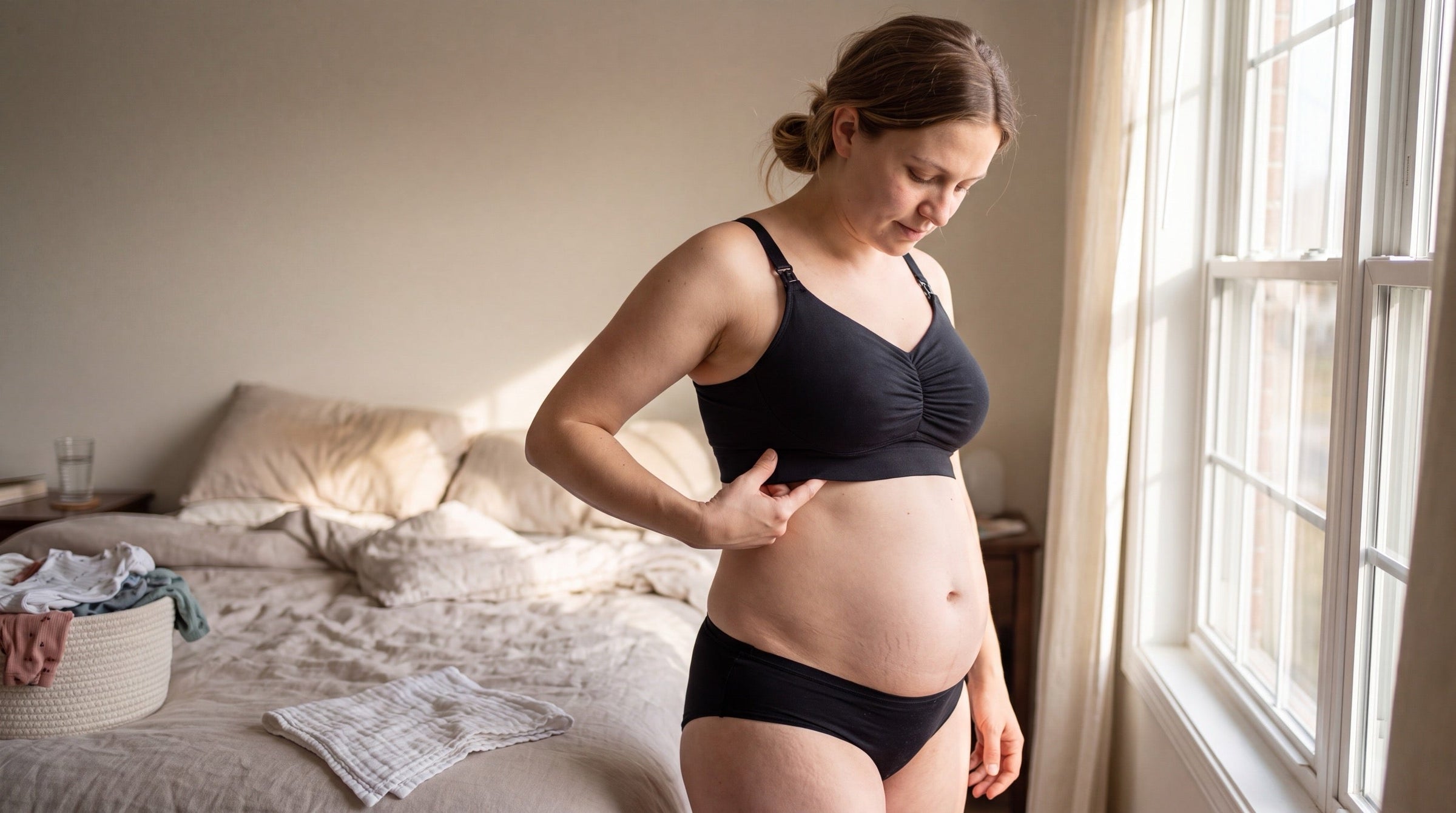 New mother a few weeks postpartum checking the fit of her black wireless nursing bra by sliding two fingers under the band, standing by a window in a lived-in bedroom